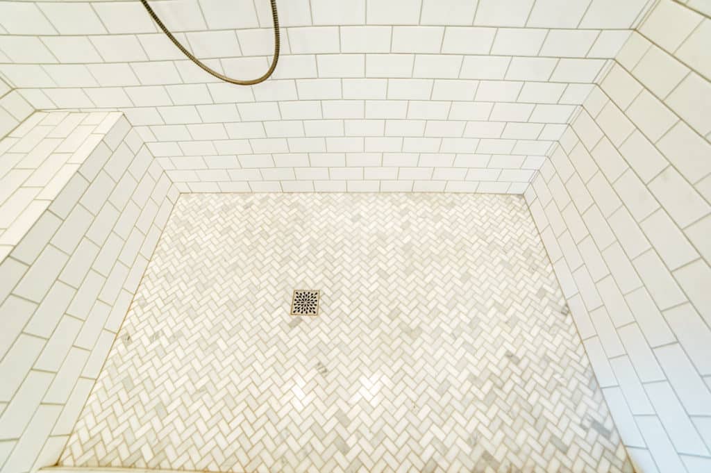 Marble herringbone tile shower floor with classic white subway tile walls.