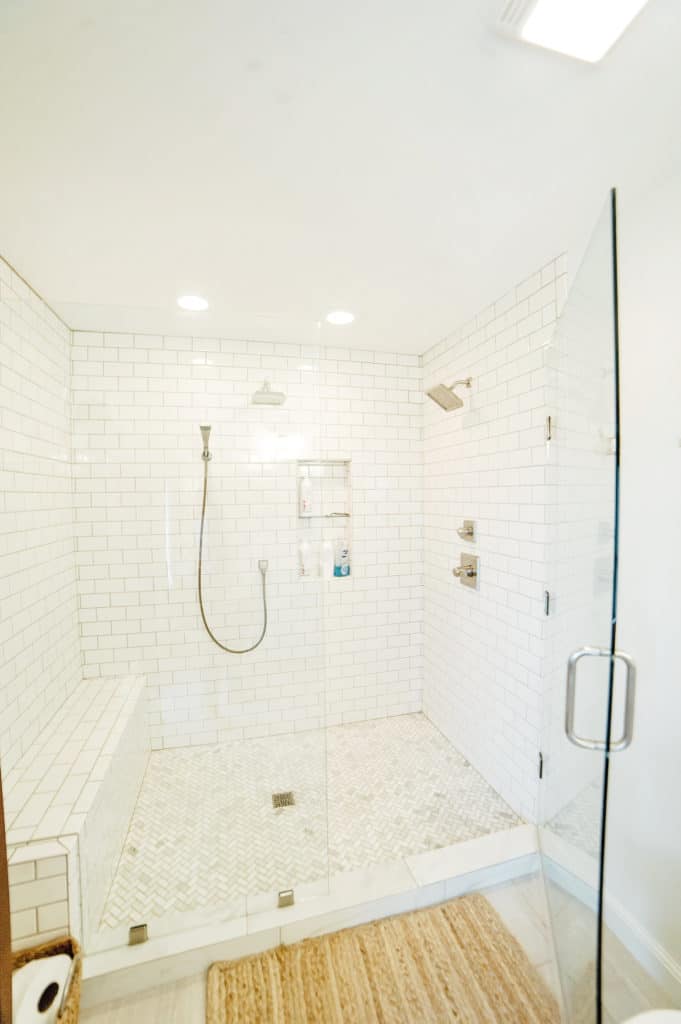 Huge walk-in shower featuring white subway tile, marble herringbone tile floor and dual shower heads and body spray!