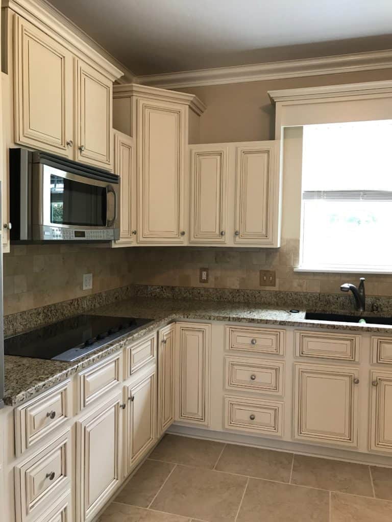 Creamy off white painted kitchen cabinets with brown glaze. Gorgeous granite and tumbled travertine tile backsplash.