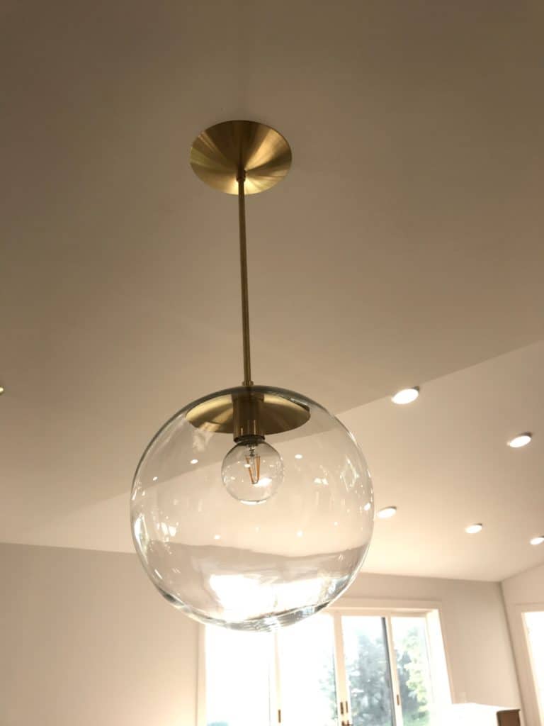 Large Mid Century Modern inspired brass and clear glass globe pendant over kitchen island.