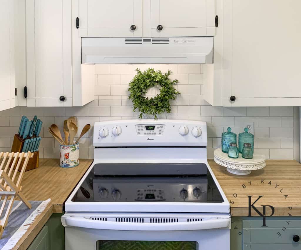 white upper cabinets and green bottom cabinets, white appliances with painted cabinets, faux wreath above stove