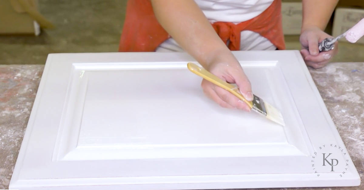 Painter using a brush to tip off paint that was rolled on a cabinet door.