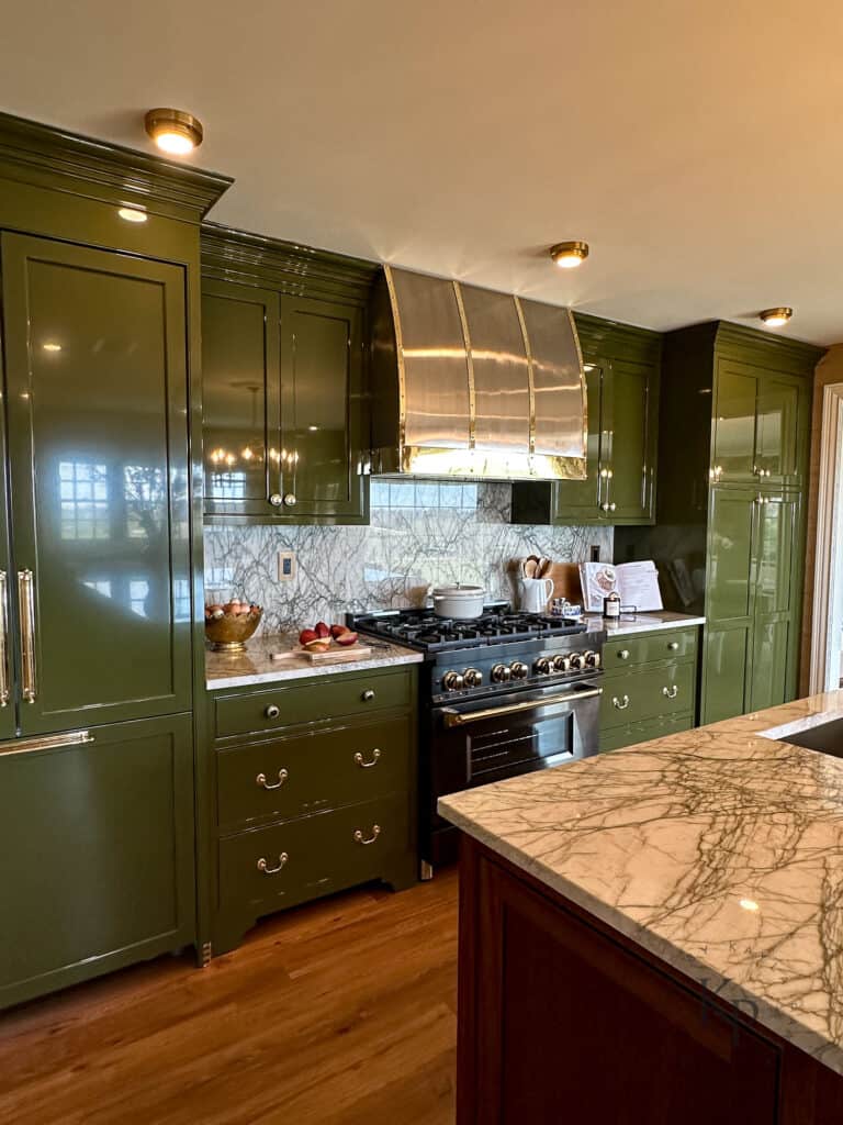 dark green kitchen cabinets. lacquered cabinets. stainless steel and brass range hood over black range